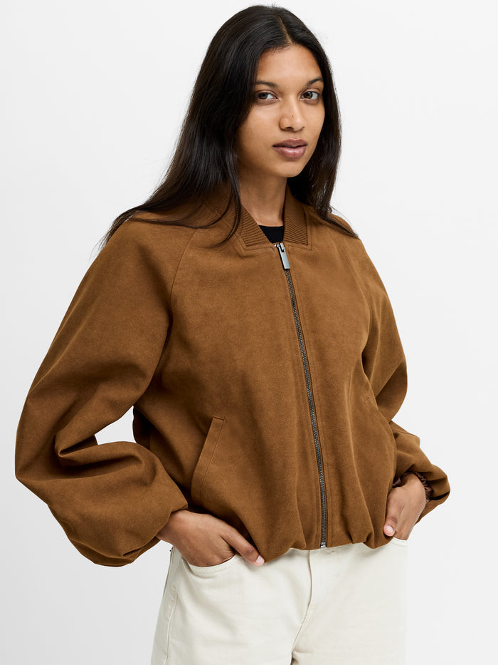 A woman wearing a brown suede Bomber jacket with long batwing sleeves, a zip through fastening, a ribbed bomber collar and 2 side pockets.