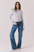Full body view of woman wearing Chaser’s Owen Moonstone Grey Long Sleeve top and blue jeans on a light gray background