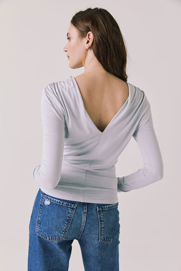 Back view of woman wearing Chaser’s Owen Moonstone Grey Long Sleeve top featuring a low-cut open back design on a light gray background
