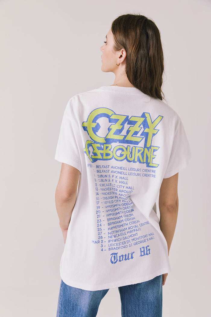 Back view of woman wearing Chaser’s white Ozzy Osbourne Tour ’86 Tee featuring “OZZY OSBOURNE” text, tour dates, and “TOUR 86” lettering on a plain background