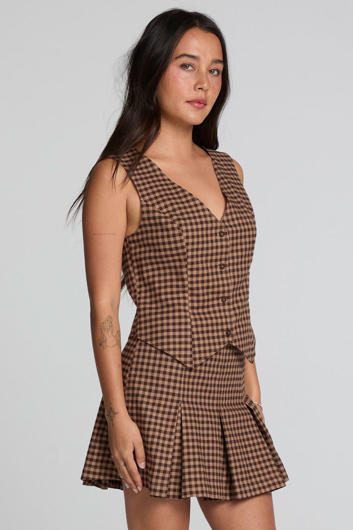 Side angle view of a woman wearing the Chaser Pea Choco Check Waistcoat and matching skirt on a neutral background