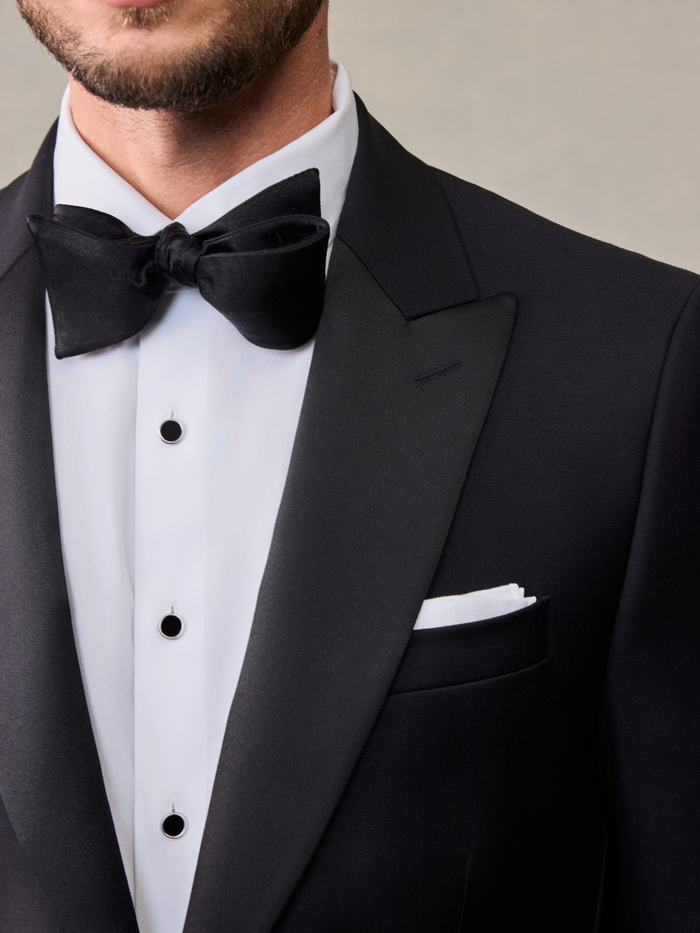 Close-up of black bow tie and peak lapel on tuxedo jacket, white shirt with black studs