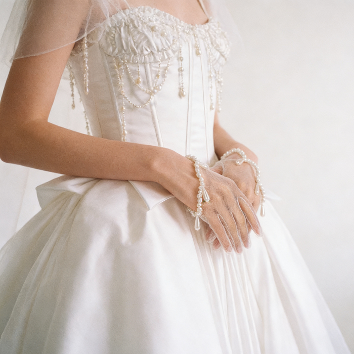 Pearl bridal wrist gloves crafted from illusion tulle with hand sewn faux pearls and a wave-shaped cuff.