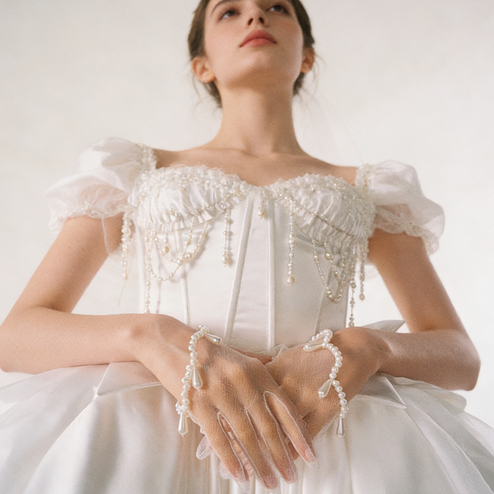Bride wearing pearl embellished illusion tulle wrist gloves with a wedding gown during an elegant bridal ceremony.