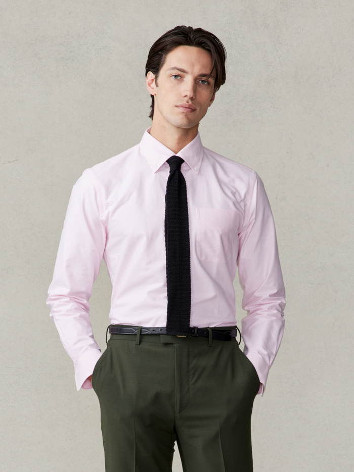 Man in pink oxford shirt and olive trousers with black knit tie, hands in pockets