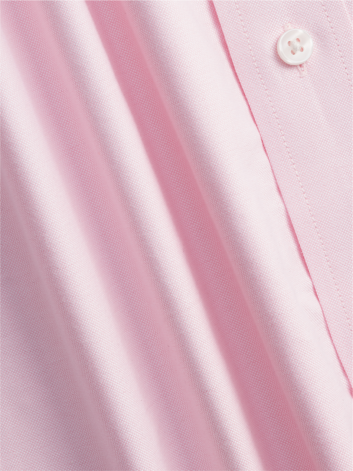 Close-up of pink oxford shirt fabric texture with button, diagonal folds