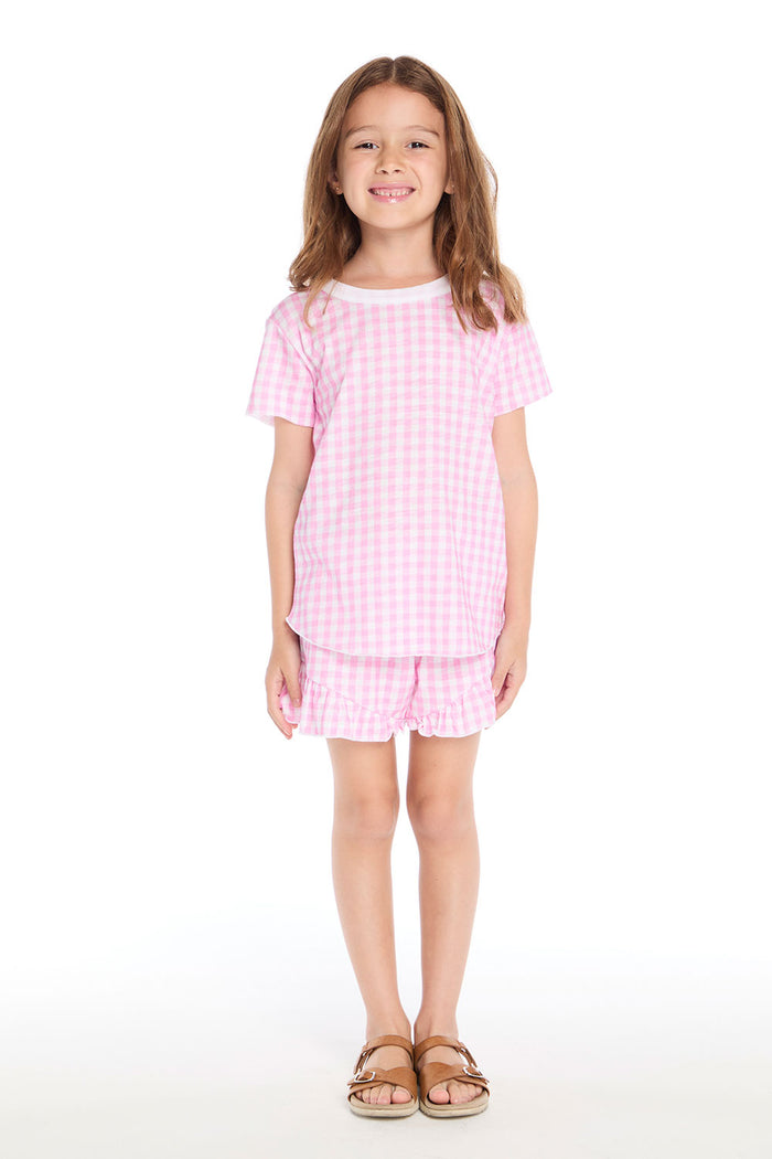 Girl wearing the Chaser Kids Pinky Gingham Grotto Shorts paired with the matching Pinky Gingham Short Sleeve Shirttail Tee and sandals on a white background