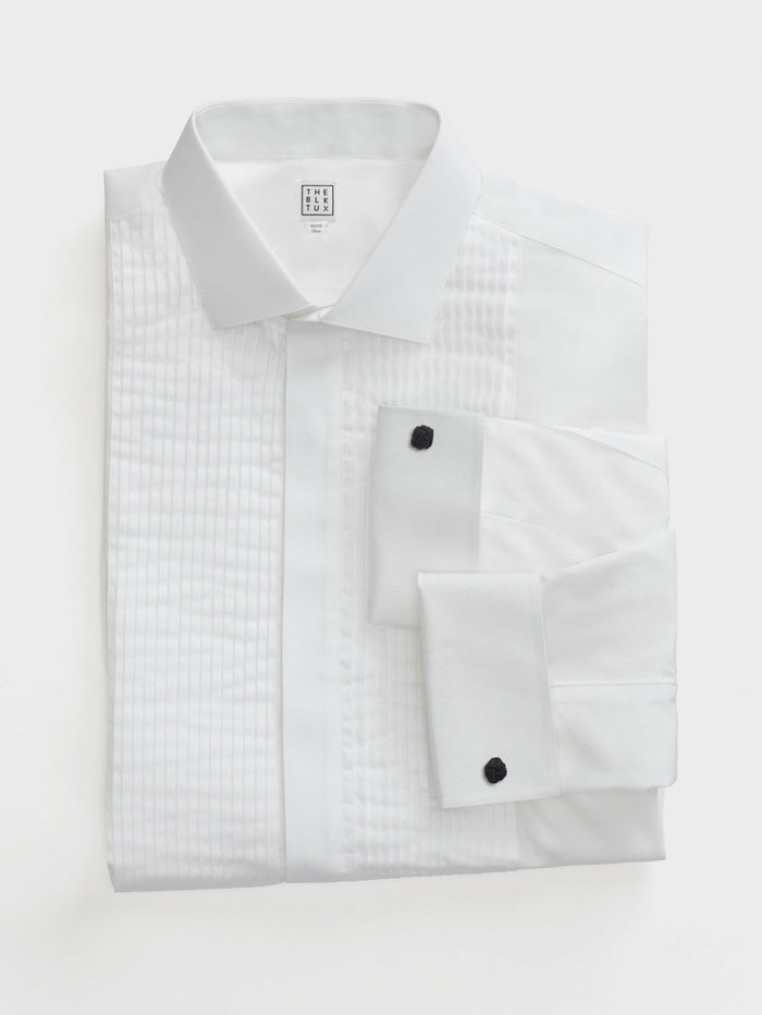White pleated tuxedo shirt with black studs, folded flat, on light grey background