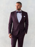 Man in plum shawl lapel tuxedo suit, hand in pocket, looking aside, grey backdrop