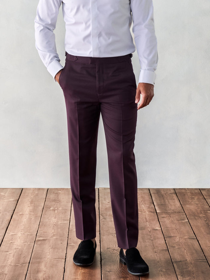 Close-up of plum tuxedo trousers on model, front view, white shirt visible, wood floor
