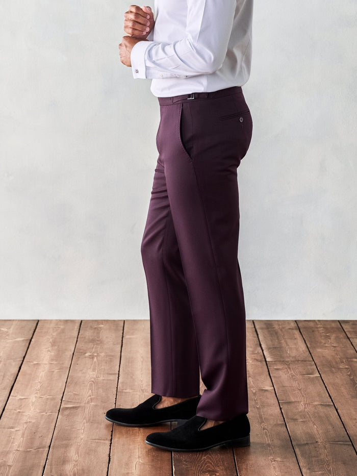 Close-up of plum tuxedo trousers on model, side view, hands clasped, wood floor