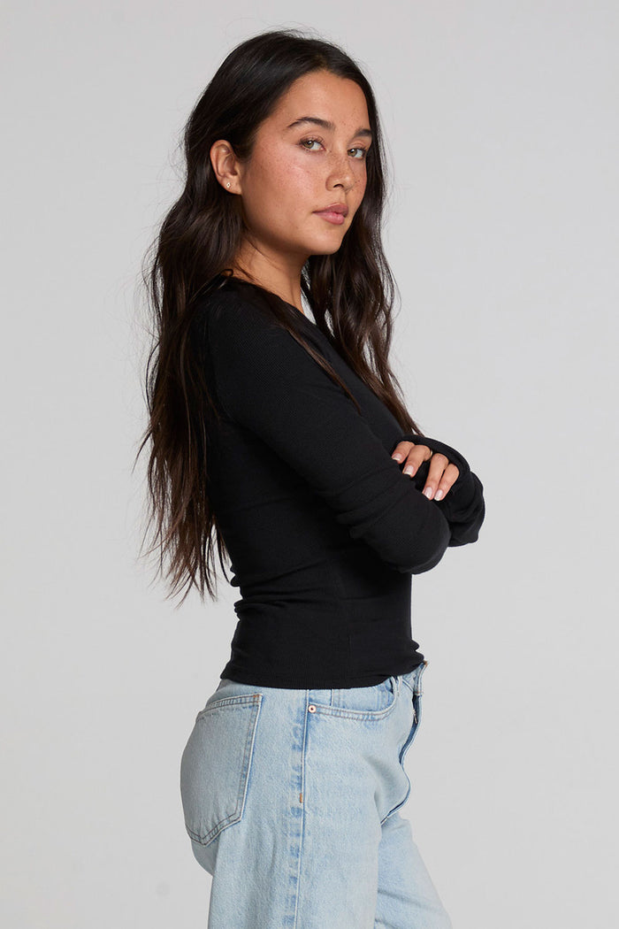 Side view of a woman wearing the Chaser Porta Black Long Sleeve on a neutral background with jeans