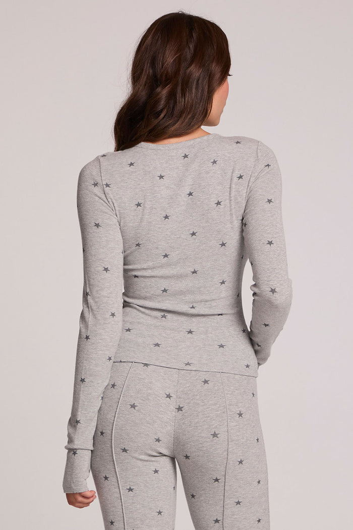 Back view of a woman wearing the Chaser Porta Light Heather Grey Long Sleeve on a neutral background with matching grey pants and hand on waist