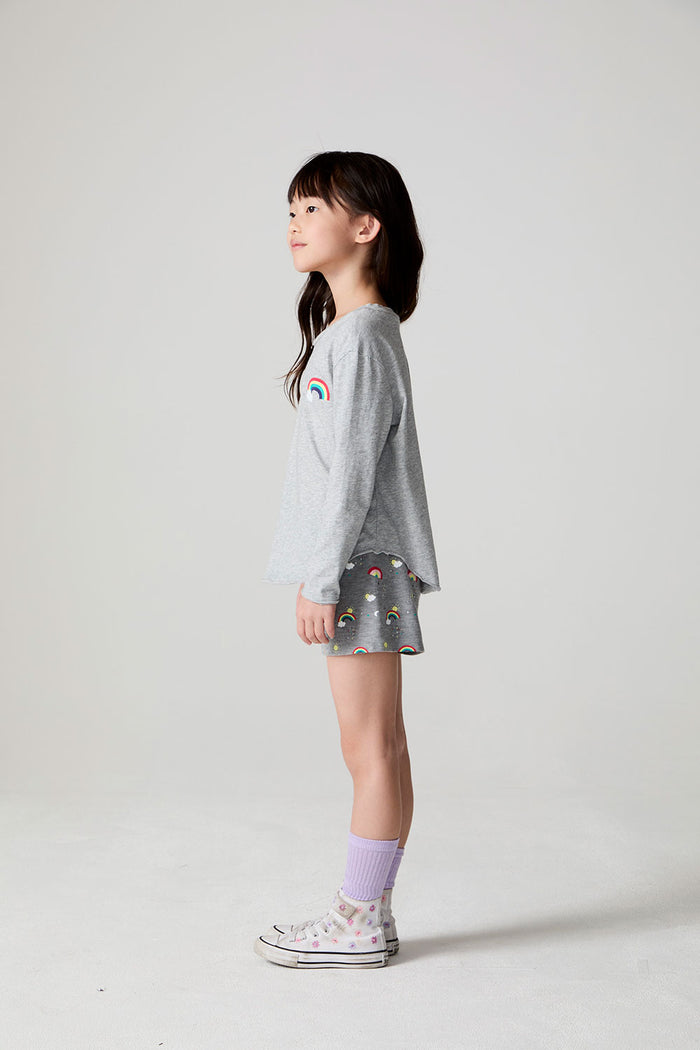 Full body side view of a girl wearing the Chaser  Rainbow Morning Allover Shorts on a neutral background