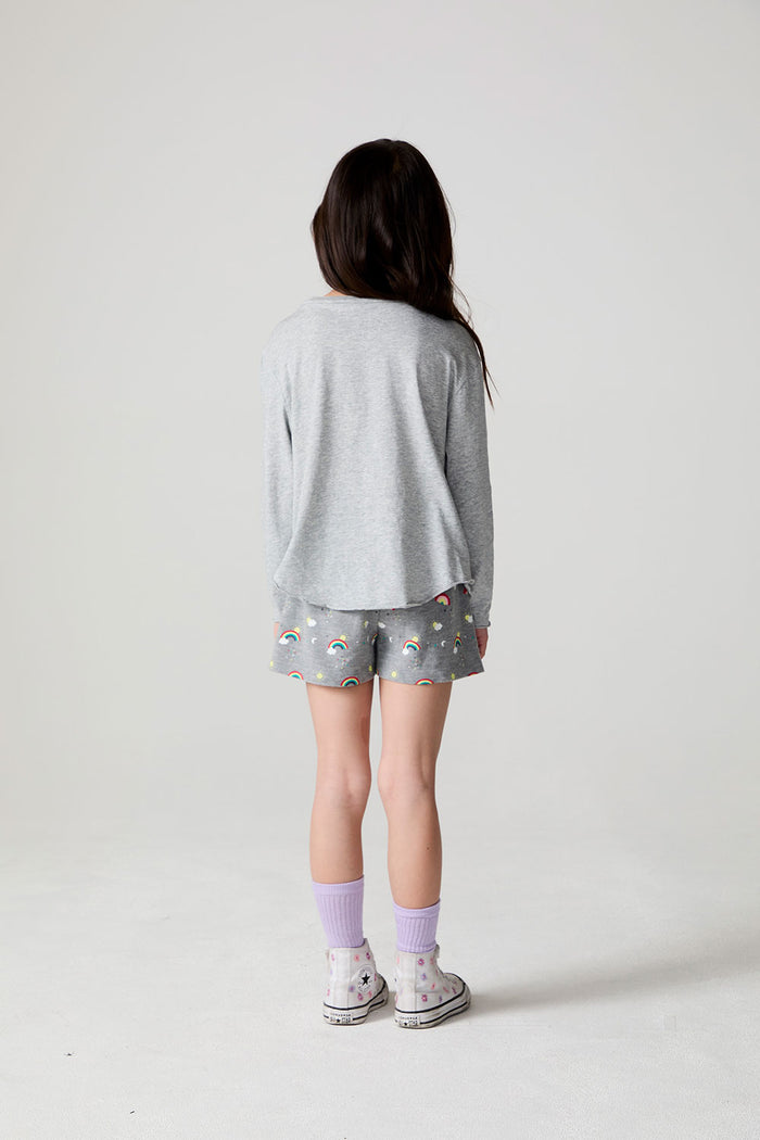 Full body back view of a girl wearing the Chaser  Rainbow Morning Allover Shorts on a neutral background
