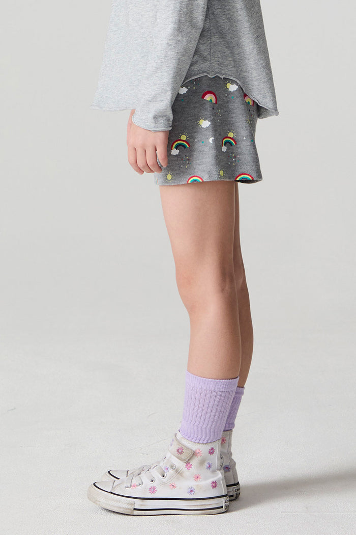 Side view of a girl wearing the Chaser  Rainbow Morning Allover Shorts on a neutral background