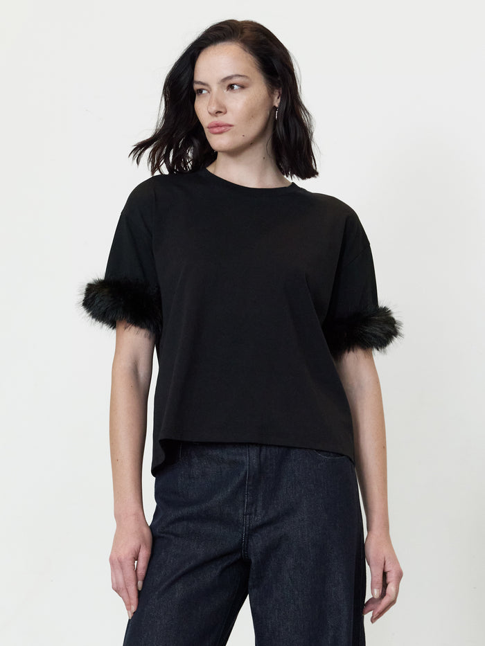 A woman wearing a black T-Shirt with drop shoulders, short sleeves with faux fur trims, a crew neckline and a relaxed silhouette.