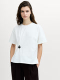 A woman wearing a white dropped shoulder short sleeved T-shirt, with a crew neck and a removable metal floral detail for a cinched fit.