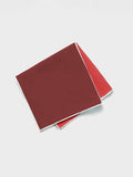 Red silk-linen pocket square folded diagonally, dark maroon top layer over coral-red underside.