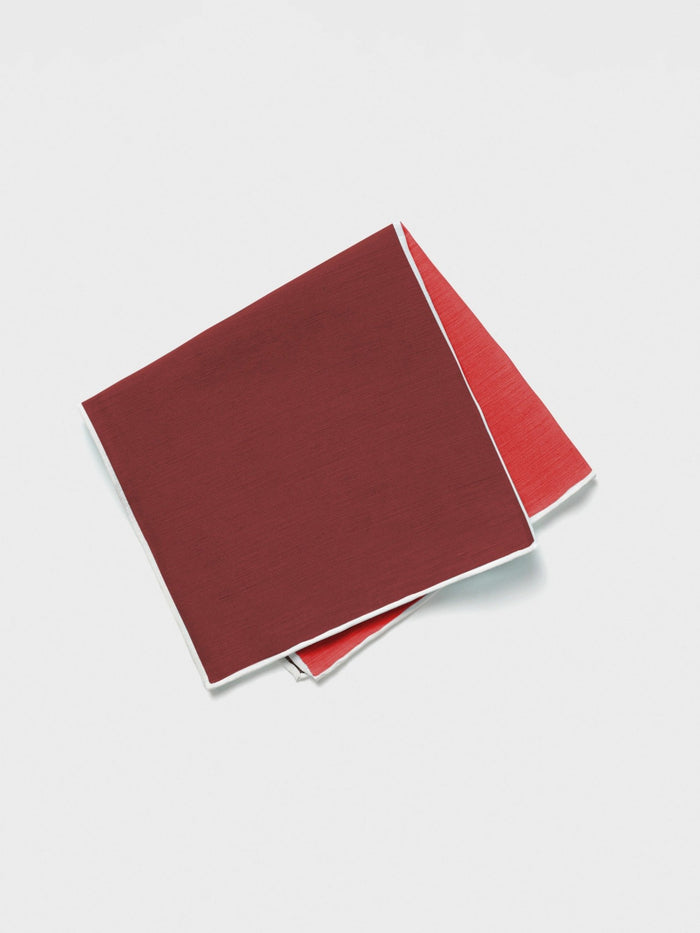 Red silk-linen pocket square folded diagonally, dark maroon top layer over coral-red underside.
