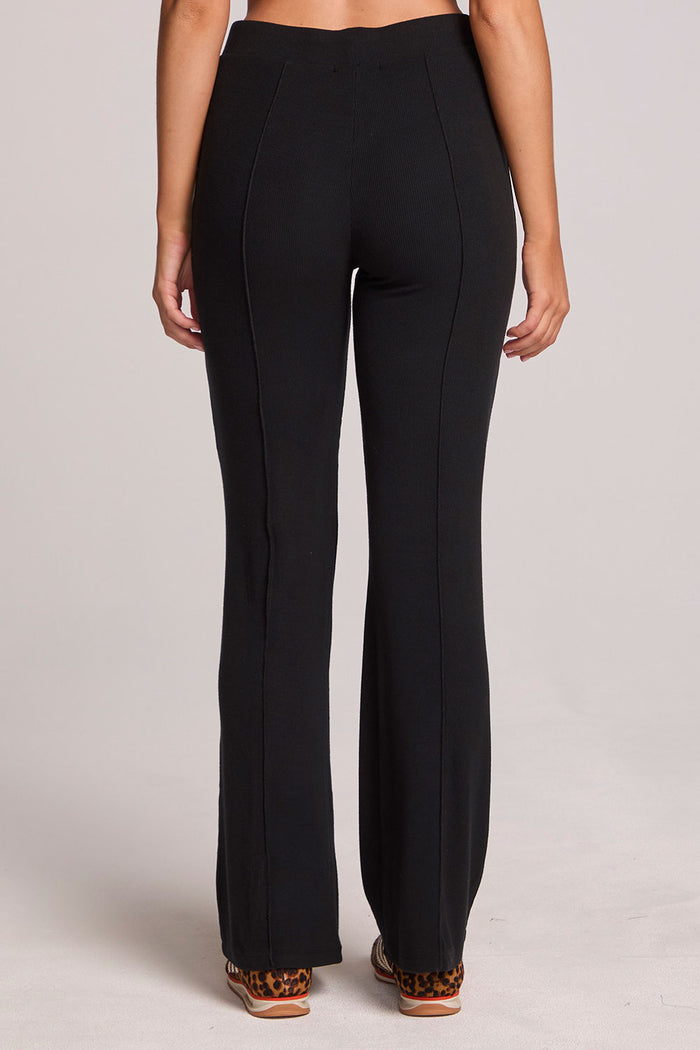 Back view of a woman wearing the Chaser Rhose Black Pants on a neutral background with arms lowered down sides