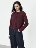 A woman wearing a knit burgundy Cardigan with long sleeves, a button down fastening, a ribbed crew neckline and 2 front pockets.