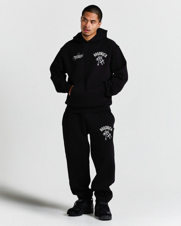 Person wearing a black hoodie and sweatpants set with visible branding on a light gray background