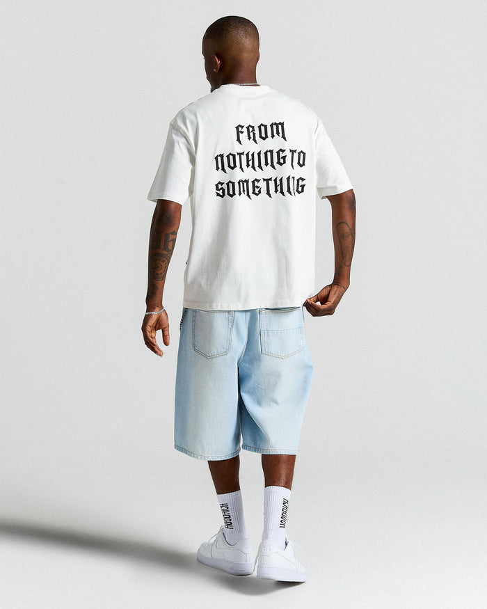 Person wearing a white t-shirt with text and light blue shorts on a plain background
