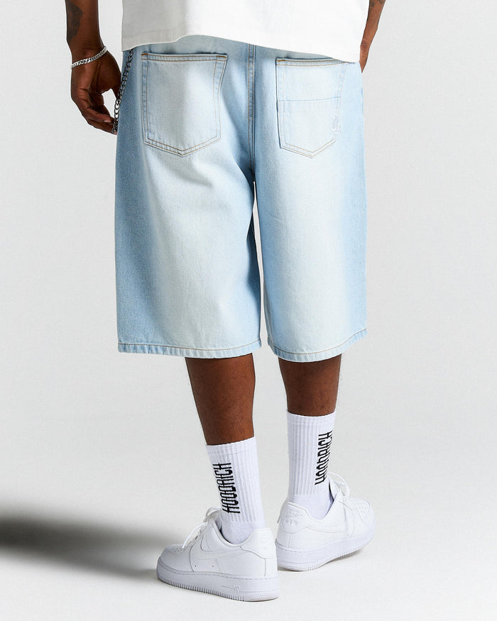 Person wearing light blue denim shorts and white sneakers on a plain background