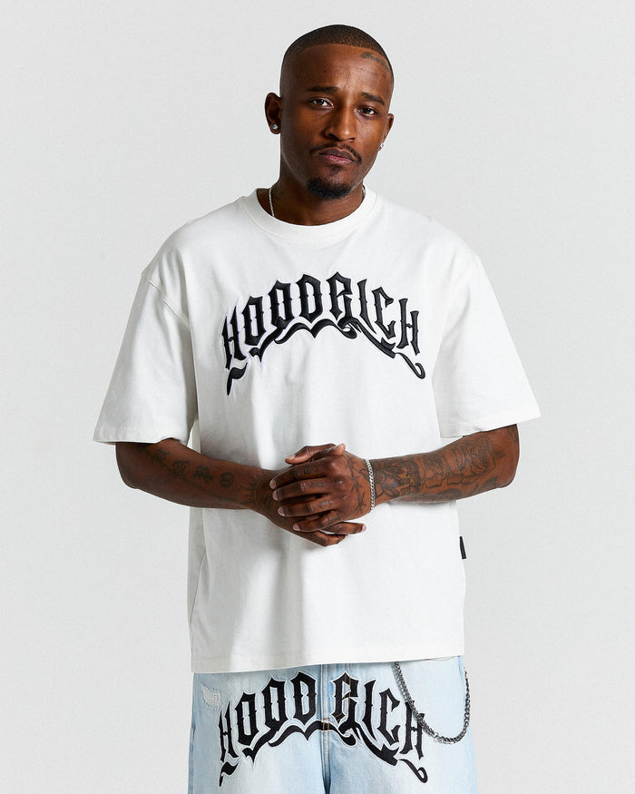 Man wearing a white 'Hoodrich' t-shirt and pants on a light gray background