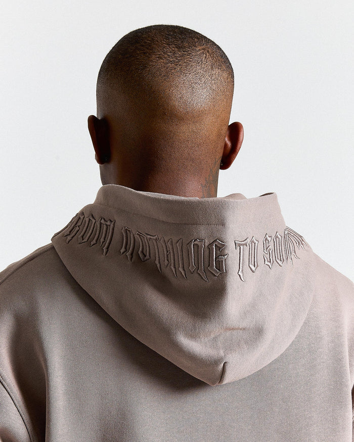Person wearing a beige hoodie with text on the back against a light gray background