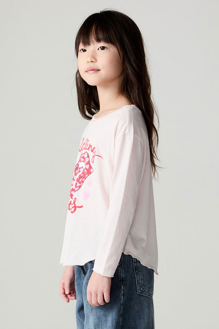 Side view of a girl wearing the Chaser Rolling Stones Luv The Stones Girls Tee on a neutral background with bluejeans