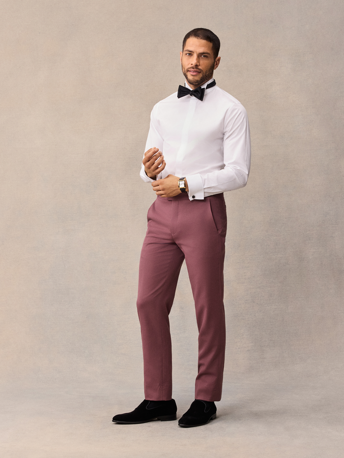 Man in white tuxedo shirt and dusty rose trousers with black bow tie, front view