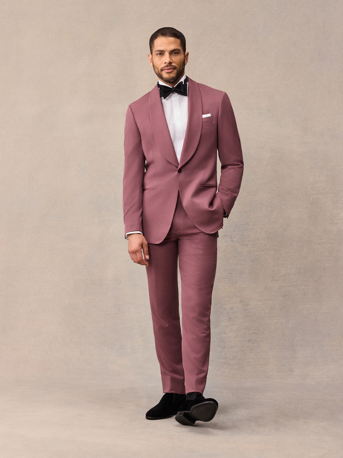 Man in dusty rose shawl collar tuxedo suit with black bow tie, standing, on beige backdrop