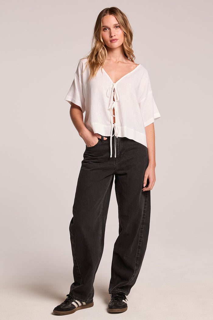 Side angle view of a woman wearing the Chaser Roselie White Blouse and black pants and shoes on a neutral background