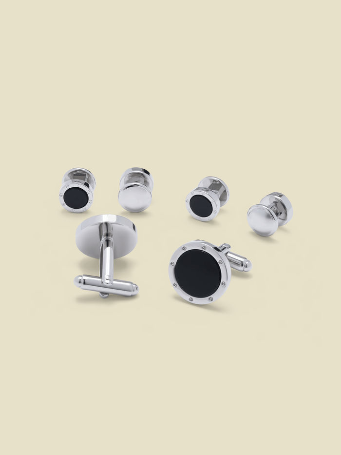 Silver cufflinks and shirt studs with black obsidian centers and rivet detail, beige background