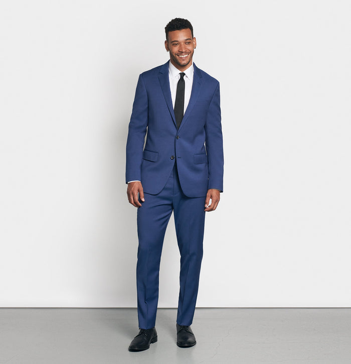 Man in royal blue suit and black tie, front view, smiling, on light grey background