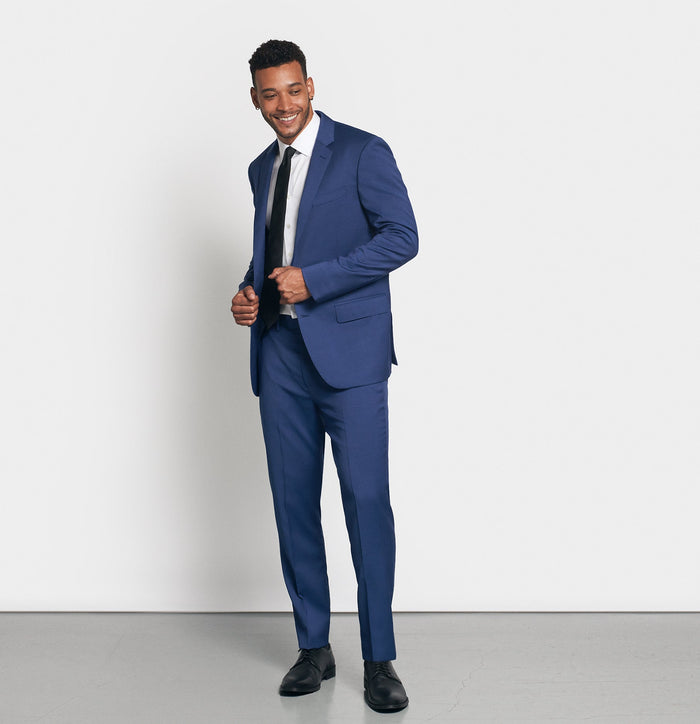 Man in royal blue suit and black tie, three-quarter view, smiling, looking down