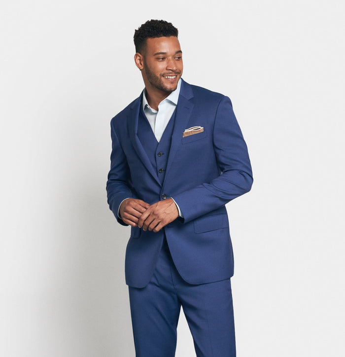 Man in royal blue three-piece suit with tan pocket square, smiling, buttoning jacket