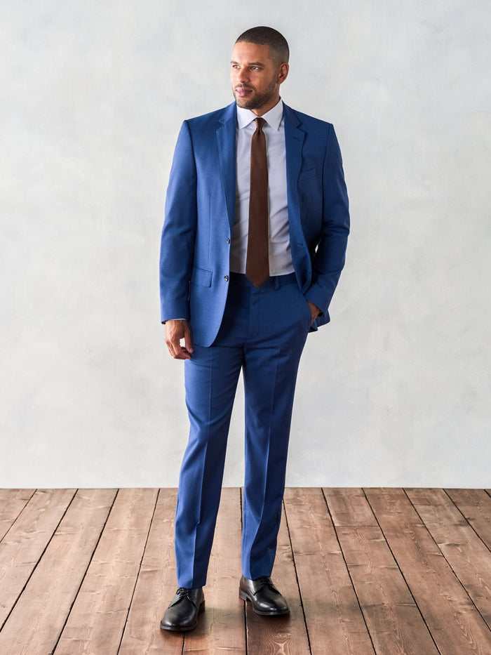 Man in royal blue suit with brown tie, full length on wood floor