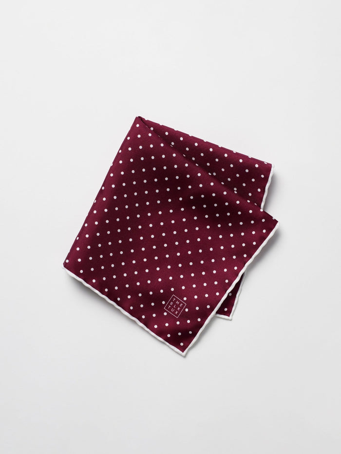 Ruby silk pocket square with white polka dots, folded diagonally on a grey background.