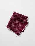 Ruby silk pocket square with white polka dots, folded diagonally on a grey background.