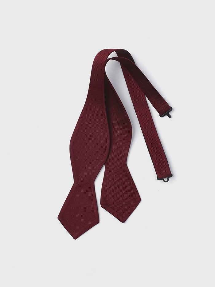 Ruby silk self-tie diamond-point bow tie, untied and laid flat on a grey background