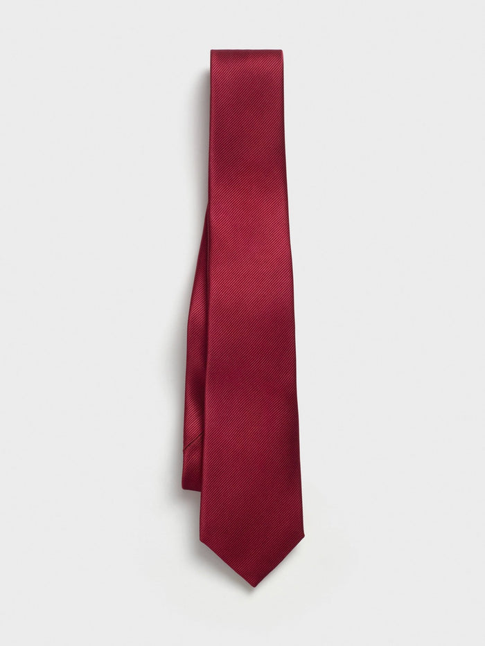 Ruby red silk necktie hanging straight and draped over itself, on a white background.
