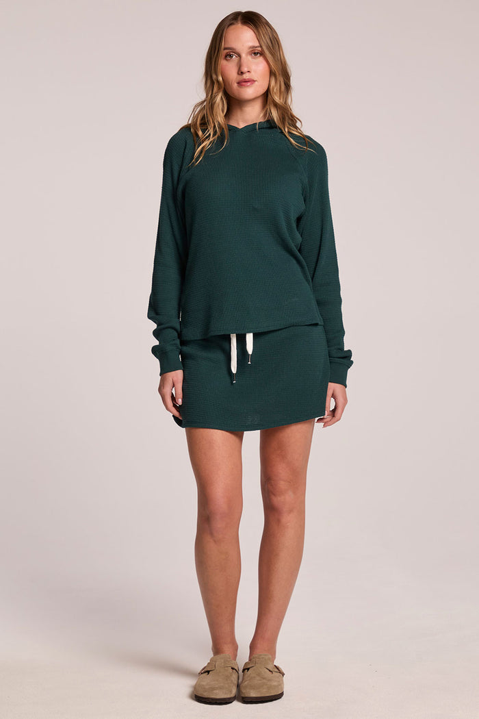A full body front view of a woman wearing the Chaser Ruee Pine Green Skort and matching top on a neutral background
