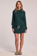 A full body front view of a woman wearing the Chaser Ruee Pine Green Skort and matching top on a neutral background