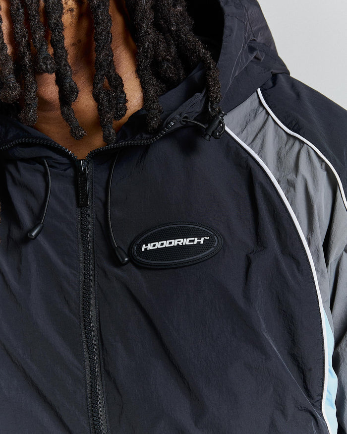 Person wearing a black and gray jacket with 'Hoodrich' logo on a neutral background