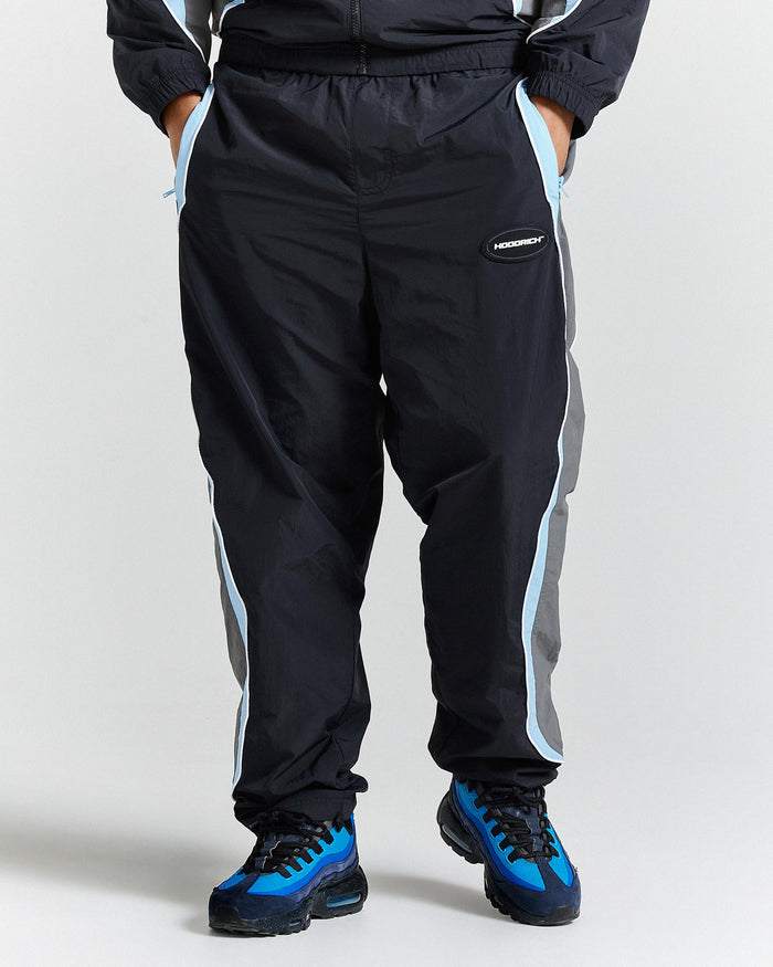 Person wearing black tracksuit with white and blue stripes on a plain background