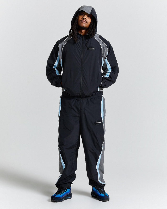 Person wearing a black and gray tracksuit with blue accents on a white background