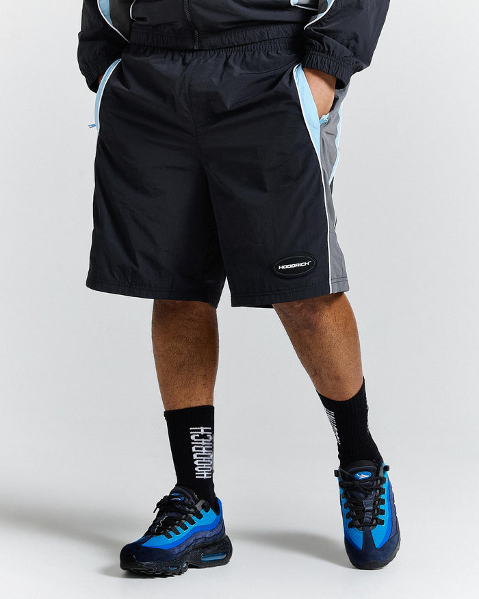 Person wearing black athletic shorts and blue sneakers on a white background